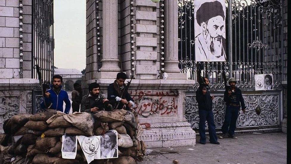 Armed men stand guard outside a Tehran building which has a poster of Khomeini hanging from the gate
