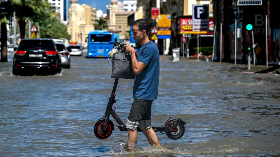 Čovek koji nosi skuter sa vodom do kolena u Dubaiju