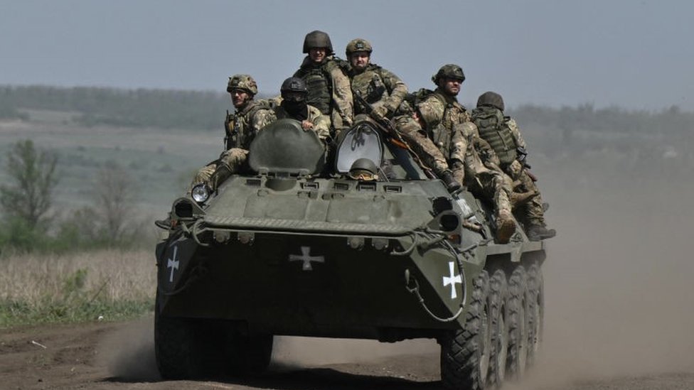Ukrainian servicemen ride on an armored personnel carrier (APC) in a field near Chasiv Yar