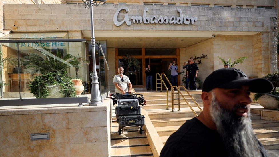 Izrael i Palestinci: Granični prelaz Rafa zatvoren, UN upozorava da je „Gaza na ivici gladi" 10 A man pushing a cart carrying media equipment out of the Ambassador Hotel in Jerusalem while five people stand near the entrance