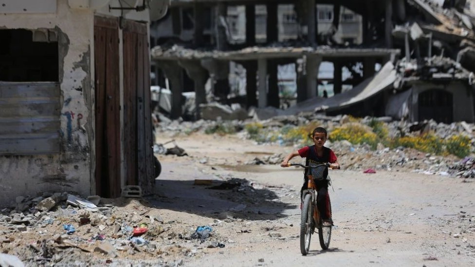 Izrael i Palestinci: Izraelu nedostaje plan za „dan posle" rata u Gazi 1 A boy on a bicycle with destroyed buildings behind him in the Az-Zaytoun neighbourhood in Gaza City