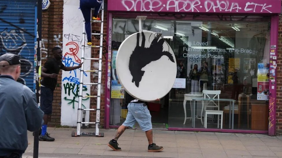 Velika Britanija i umetnost: Ukraden Benksijev vuk koji zavija 2 Muškarac nosi satelitsku antenu sa umetničkim delom niz ulicu