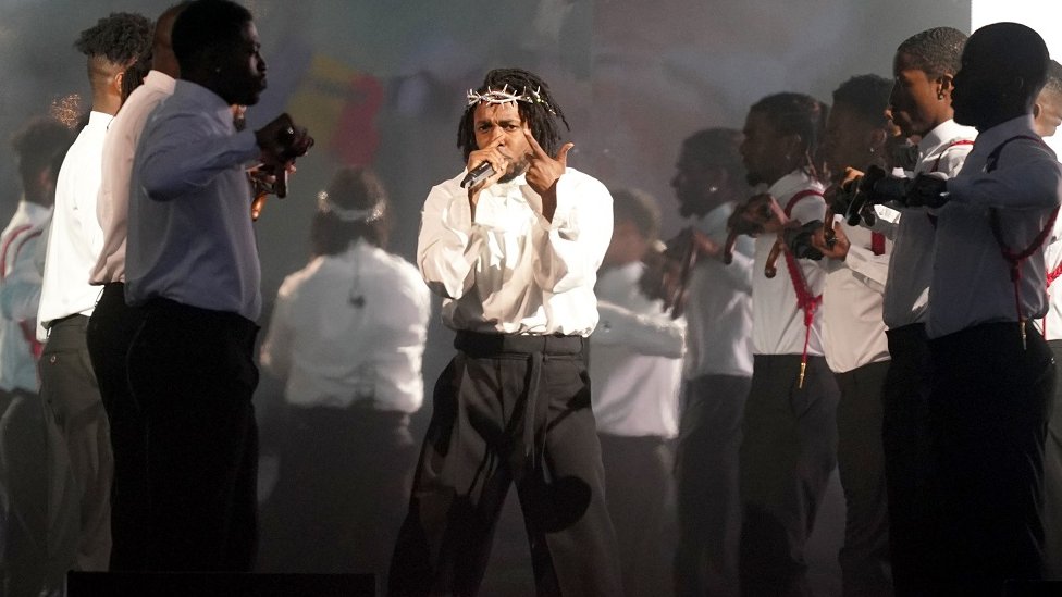 Superboul 2025: Kendrik Lamar nastupa tokom polufinala najvećeg takmičenja u američkom fudbalu 1 Kendrik Lamar u beloj košulji i crnim pantalonama sa žicom oko glave tokom nastupa na Glastonburiju