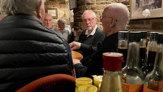 Četvrtak je za drugare i pivo: Nisu propustili okupljanje 56 godina 3 A group of gentlemen in their eighties sit chatting at a pub table. The tops of some bottles of condiments are in the immediate foreground.