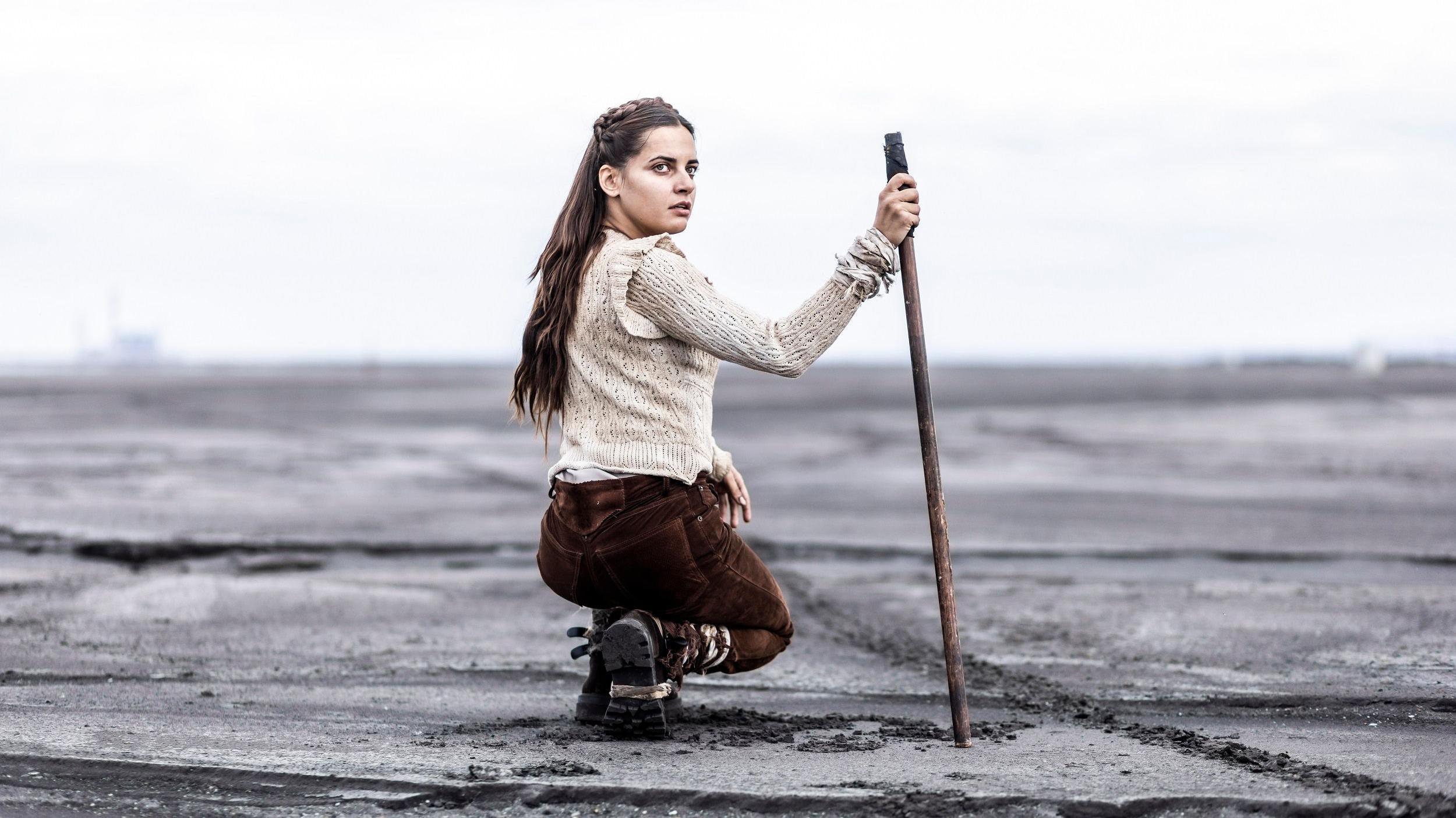 O „Volji sinovljevoj" i fantastici na domaćem filmu: Zašto partizani nikada nisu pucali u vanzemaljce 2 Devojka u čučnju u smeđim pantalonama i beloj majici okružena pustinjom drži štap u ruci i gleda u kameru - Volja sinovljeva