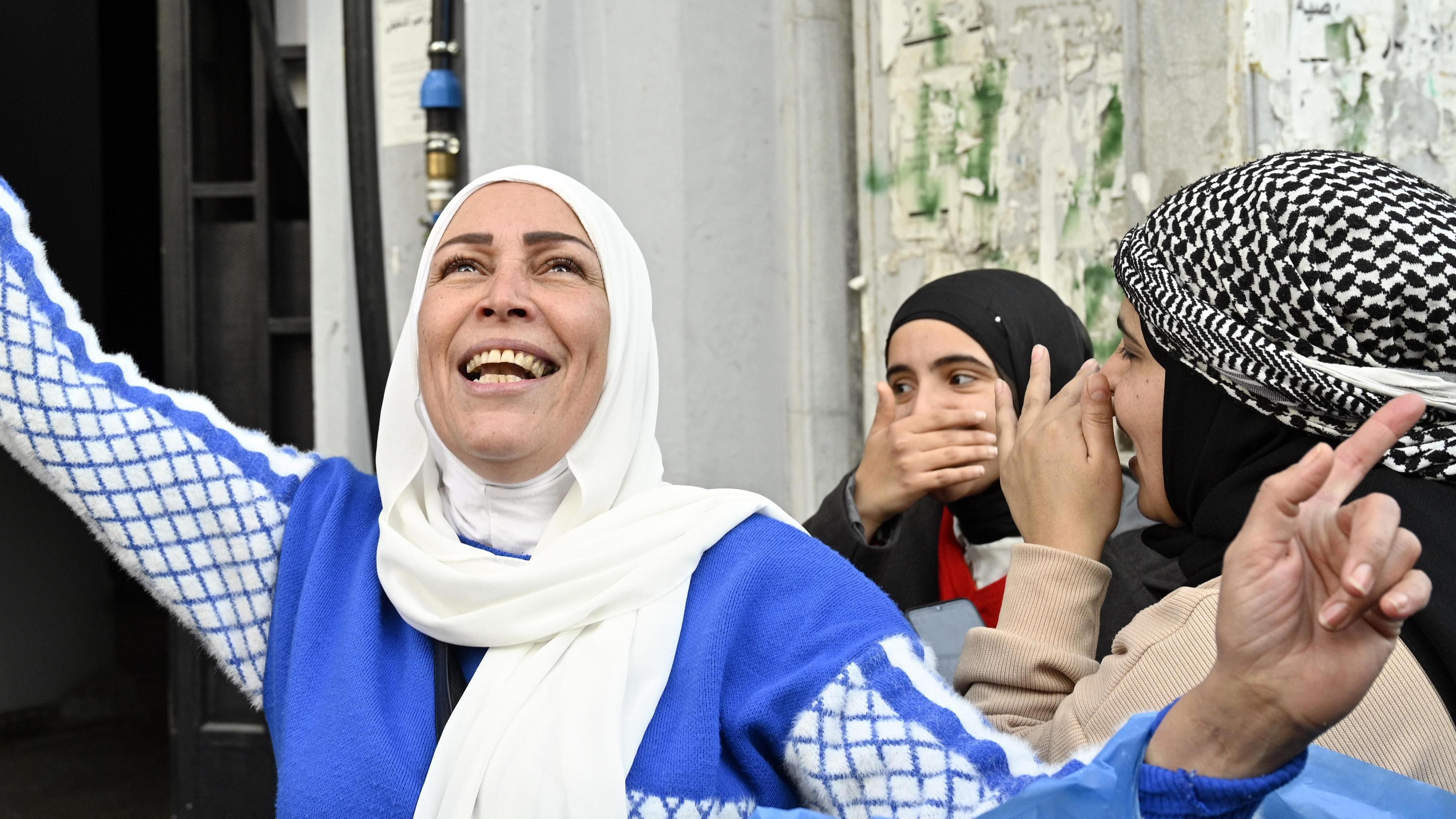 Lider HTS-a nije jedini igrač u budućnosti Sirije koja se ubrzano menja 3 A smiling woman in a blue and white dress looks up to the sky. Behind her two other women cover their smiles with their hands.