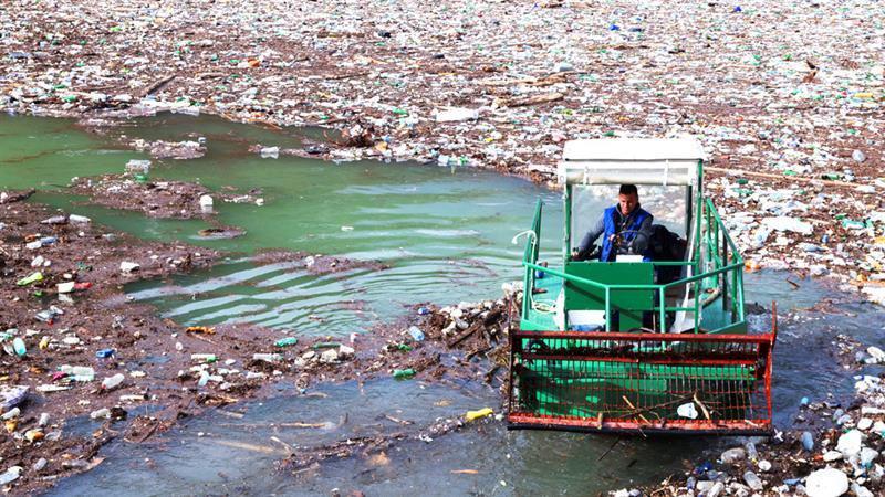 Balkanski volonteri: Pokretači „kruga dobrote” 1 Muškarac u zelenom brodu opremljenom specijalno za prikupljanje otpada skuplja smeće na vodi