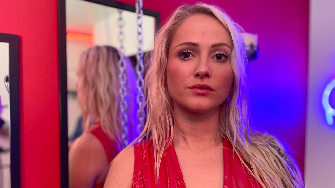 Seksualne radnice u Belgiji prve u svetu dobile porodiljsko i penziju 1 Portret Mel, koji gleda u objektiv ozbiljnog izraza lica. Ima dugačku plavu, talasastu kosu i nosi crvenu haljinu. Stoji ispred ogledala, sa zidova visi lanac, a i neonsko svetlo je u kadru