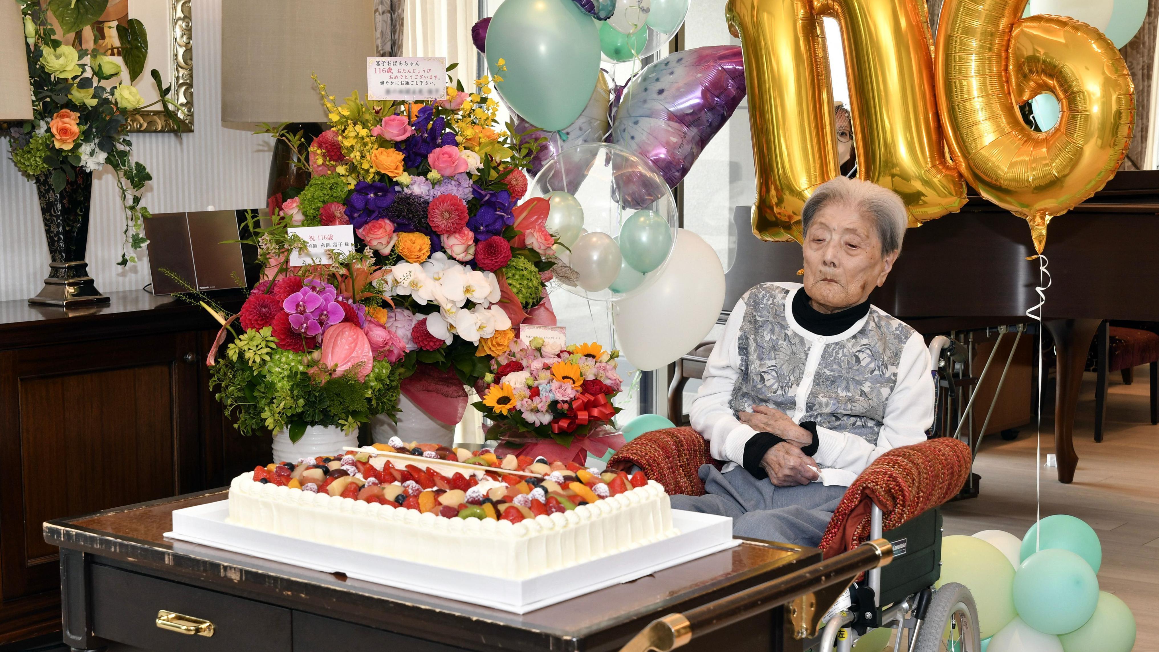 Najstarija žena na svetu preminula u 116. godini 1 Tomiko Itooka celebrates her 116th birthday. She sits in front of a large white cake topped with fruit and a bouquet of flowers. Gold helium ballons in the shapes of 116 loiter behind her.