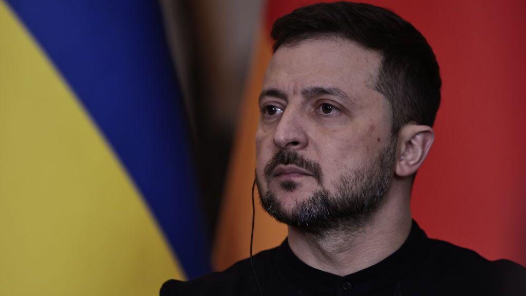 Kako bi rat u Ukrajini mogao da se okonča u 2025. 1 Volodimir Zelenski sa slušalicom u ušima, iza njega ukrajinska zastava