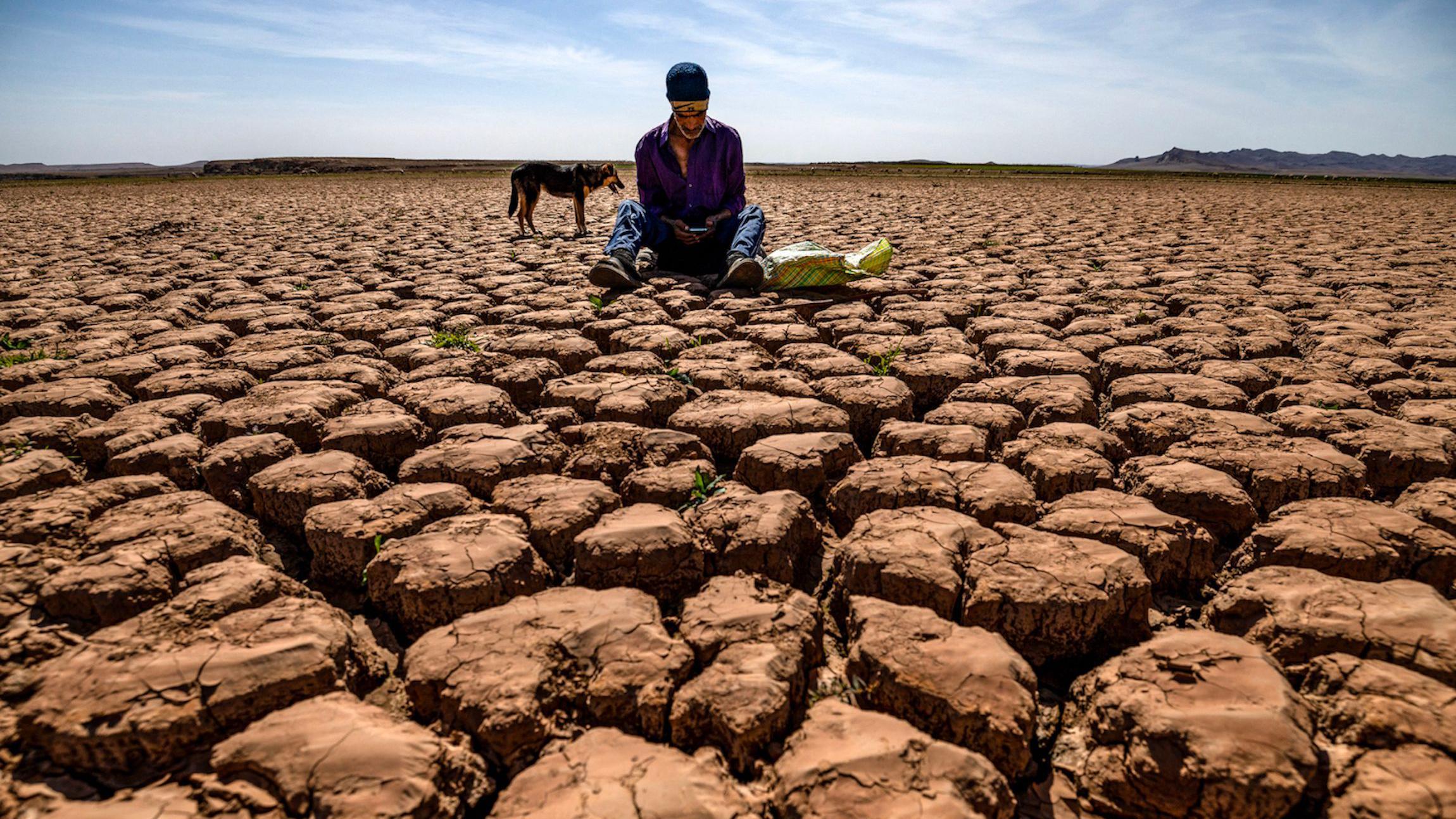 A shepherd checks his mobile phones sitting on cracked earth near Ouled Essi Masseoud in Morocco.