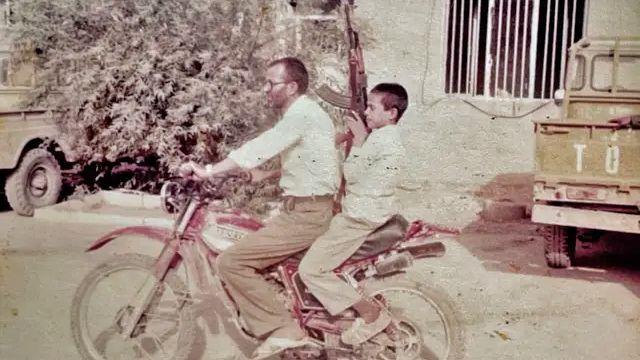 „Još imam 25 šrapnela u sebi": Bivši iranska deca vojnici otkrivaju doživotne traume 3 Reza, sa oko 11 godina, sedi na motociklu koji njegov otac vozi i drži u rukama veliku pušku