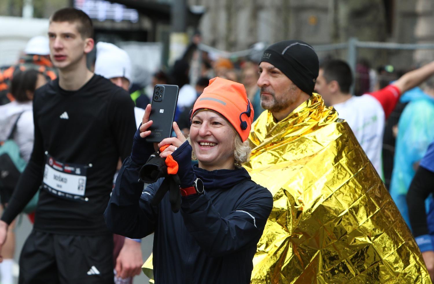 Rekordan broj učesnika, susnežica i 'Pumpaj': Beogradski maraton u fotografijama 2 žena fotografiše dok je iza nje muškarac sa pokrivačem