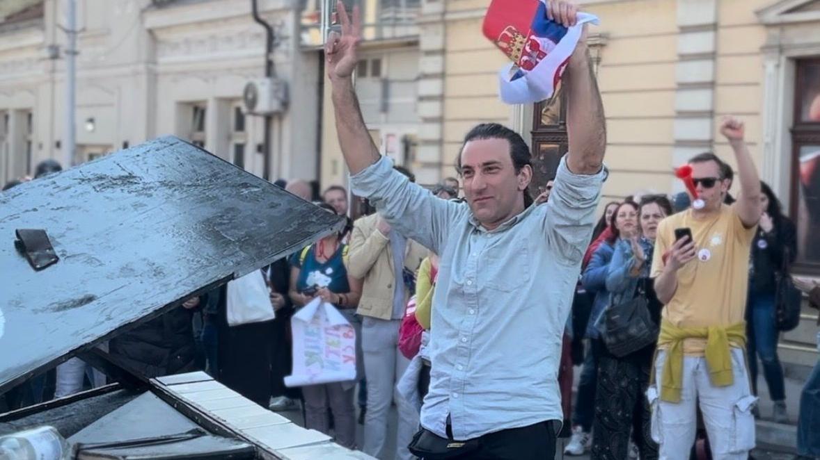 Kako su protesti u Srbiji inspirisali dvojicu italijanskih muzičara 1 David Martelo u Nišu ispred klavira sa zastavom Srbije u jednoj ruci, pokazujući tri prsta sa drugom