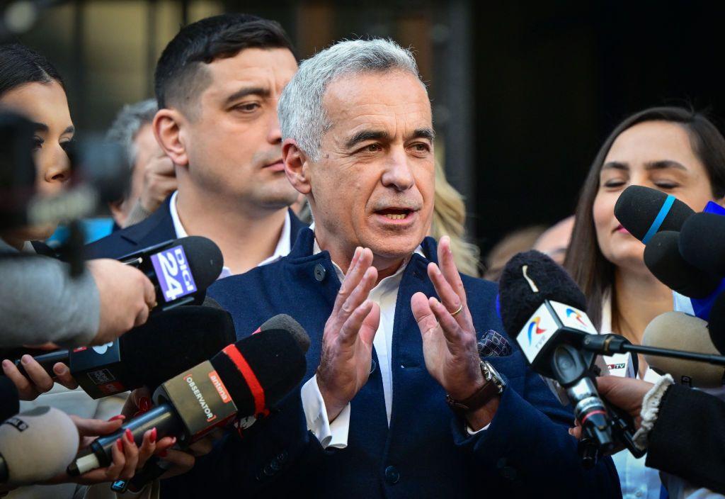 Muškarac u plavom odelu gestikulira rukama pred mikrofonima