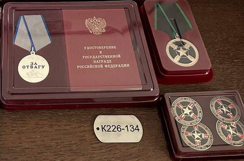 Identifikaciona pločica na kojoj piše  „K226-134" i medaljana kojoj je ugravirano „za hrabrost"  