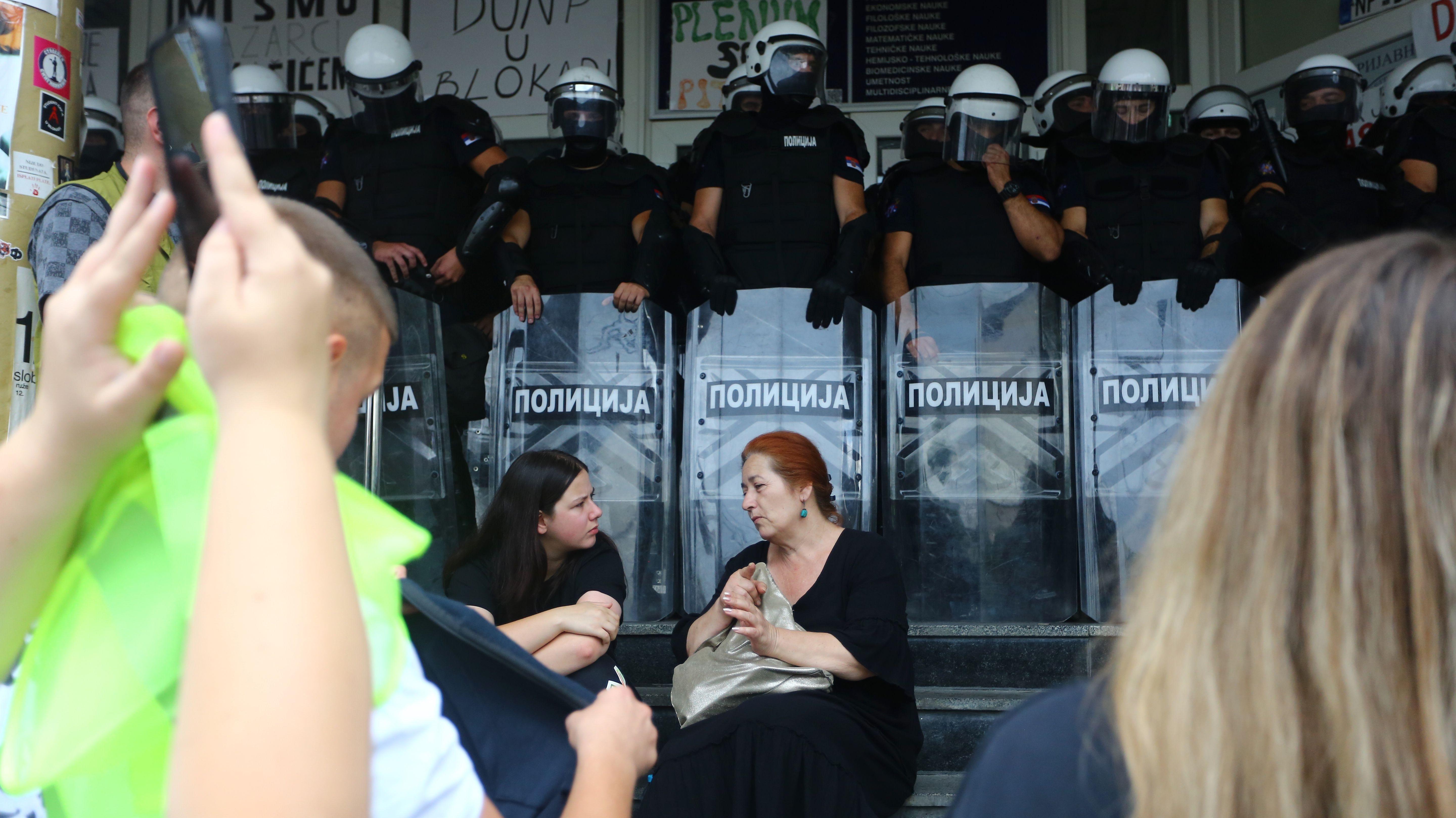 Priveden još jedan student, protesti u Novom Pazaru 4 Dve žene, obučene u tamnu odeću sede na stepenicama ispred kordona policije pod punom opremom za razbijanje demonstracija