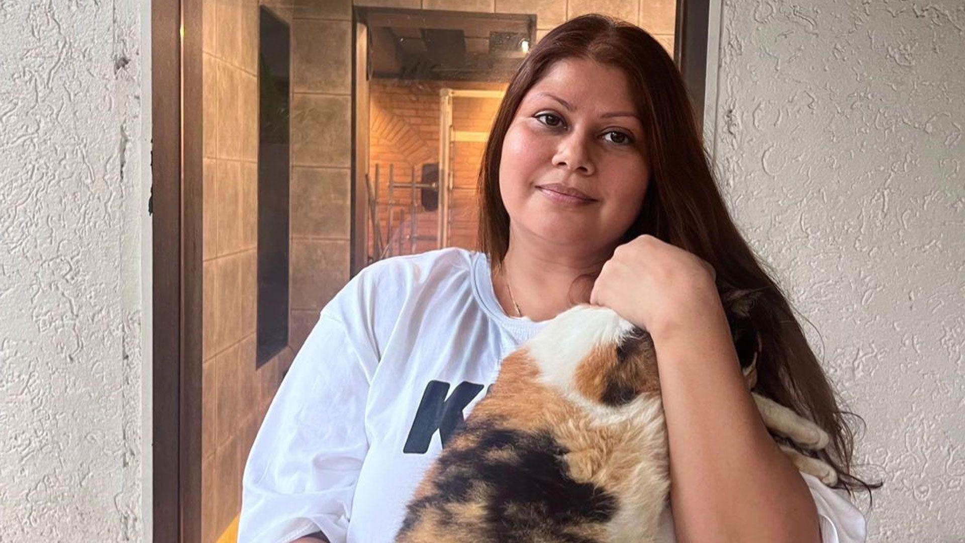 Žena sa dugom smeđom kosom, u beloj majici drži u rukama šarenu mačku