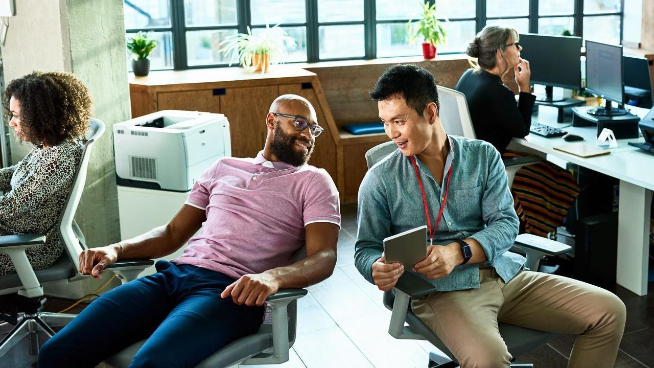 Dva muškarca sede u radnim stolicama i pričaju