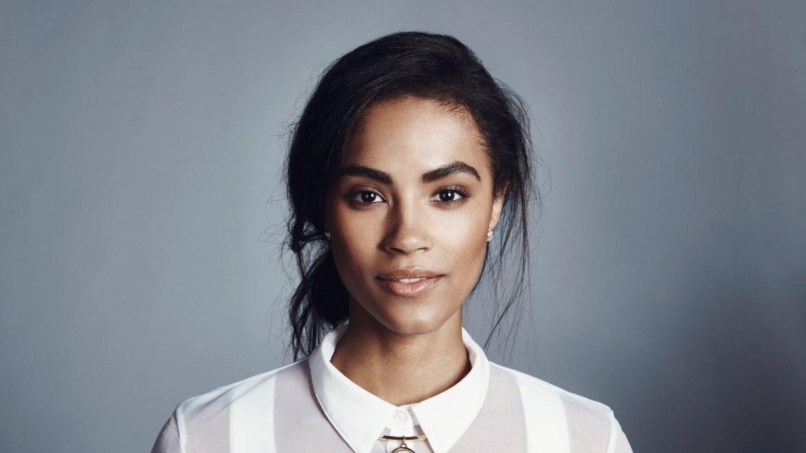 Šinejd Bojel - žena skupljene tamne kose u punđu, u beloj košulji gleda u kameru