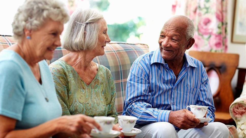 Šta nam 'supermatorci' govore o zdravom starenju 6 Dve starije žene sede na krevetu sa starijim muškarcem i drže šoljice u rukama