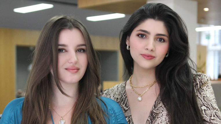 Dve devojke duge tamne kose, jedna levo u plavoj haljini, druga desno u haljini sa printom zmije