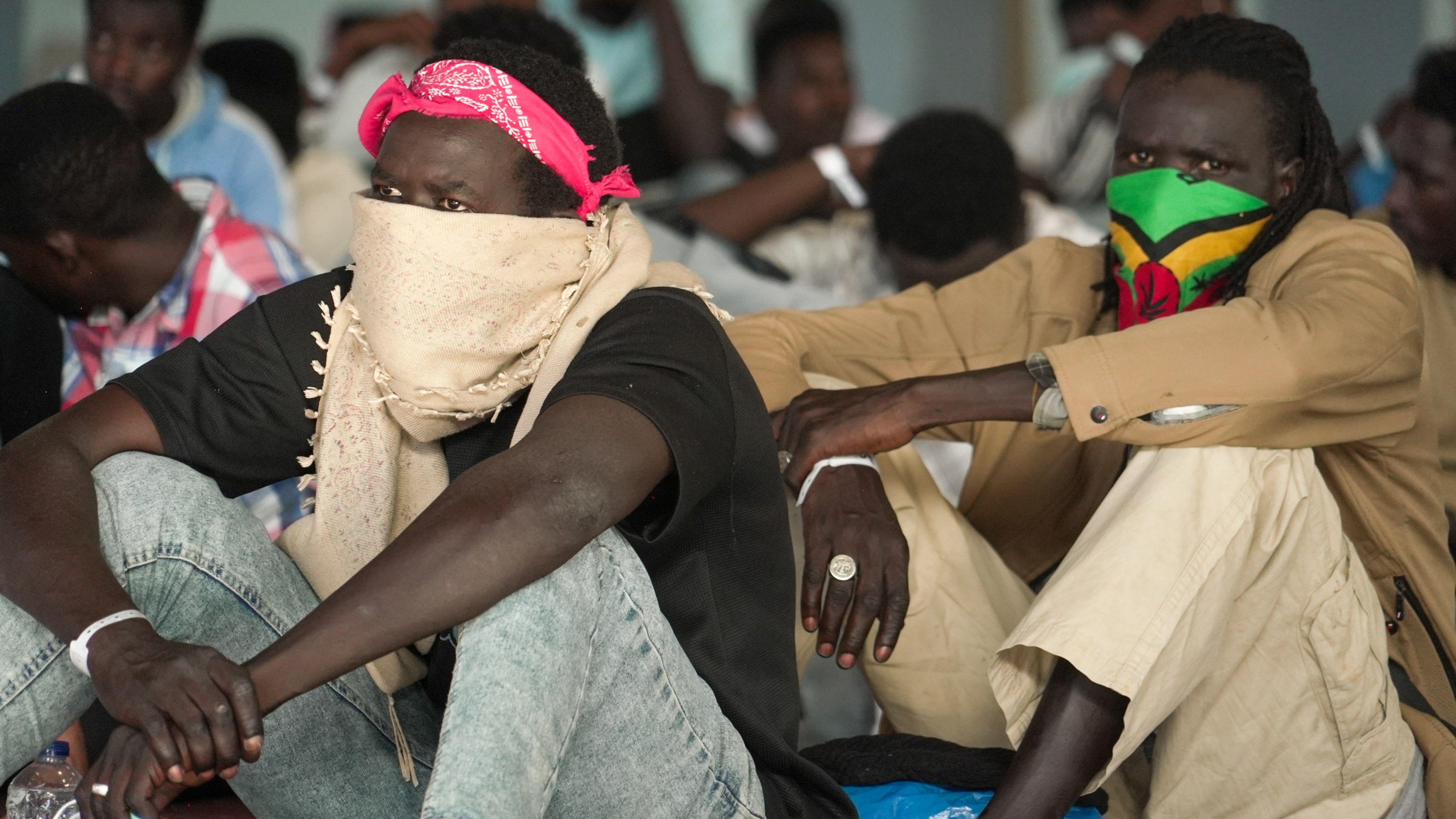 'Ovde živimo kao u zatvoru': Migranti novom rutom dolaze na Krit 1 Muškarci sede sa maramama preko lica, jedan je u farmerkama i crnoj košulji, drugi u smeđoj jakni i bež pantalonama