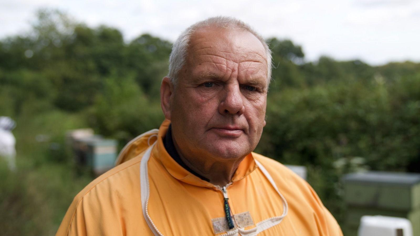 Superhrana za pčele: Nova nada za opstanak najvažnijih oprašivača 2 Muškarac nosi narandžasto pčelarsko odelo, u pozadini je zeleno drveće