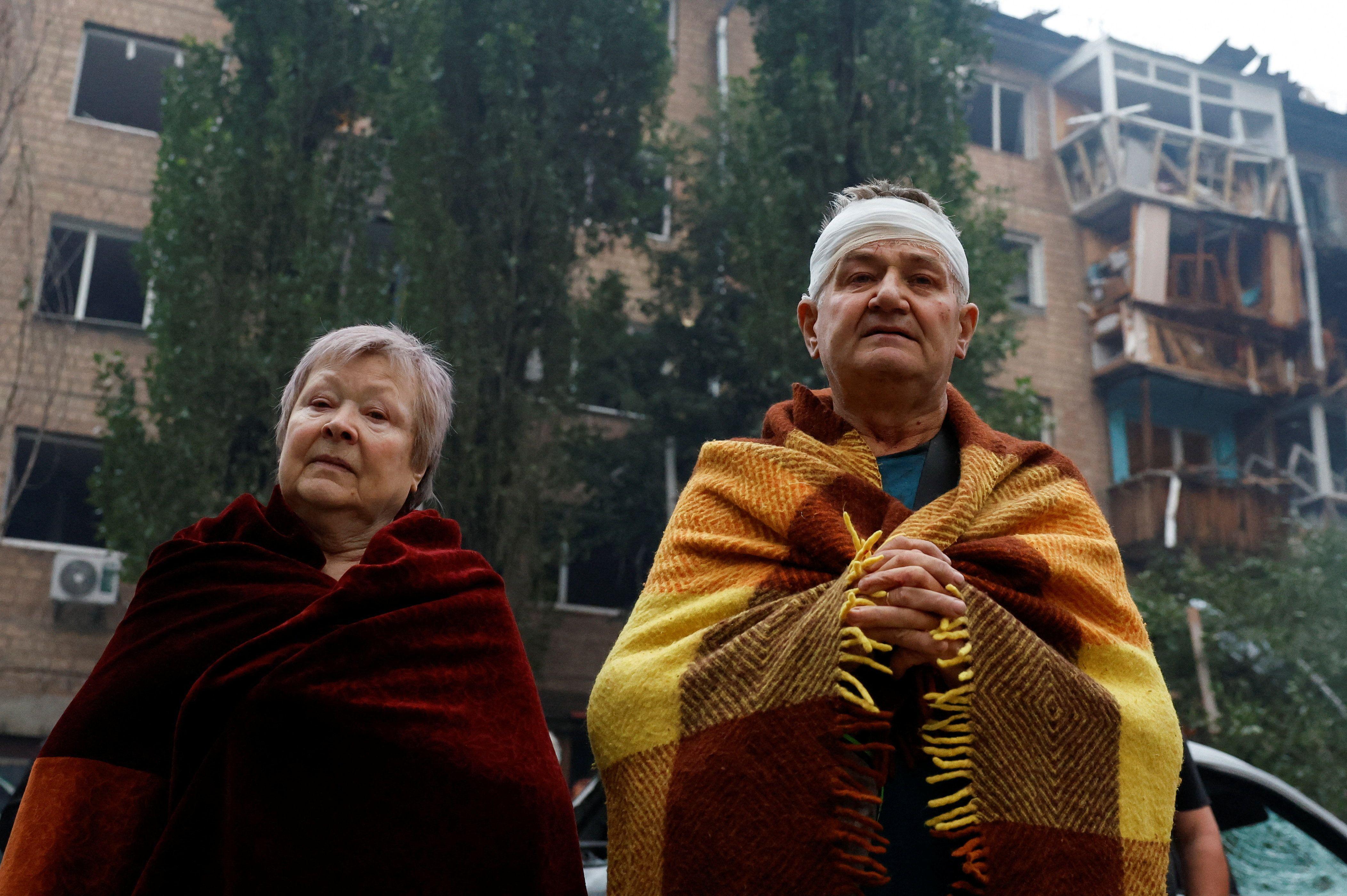Dan žalosti u Kijevu posle desetina mrtvih i ranjenih u ruskim napadima 2 Starija žena sa kratkom sedom kosom omotana ćebetom i muškarac sa zavojem preko glave, takođe omotan ćebetom, stoje napolju posle ruskih napada na Kijev. Iza njih je zgrada u ruševinama