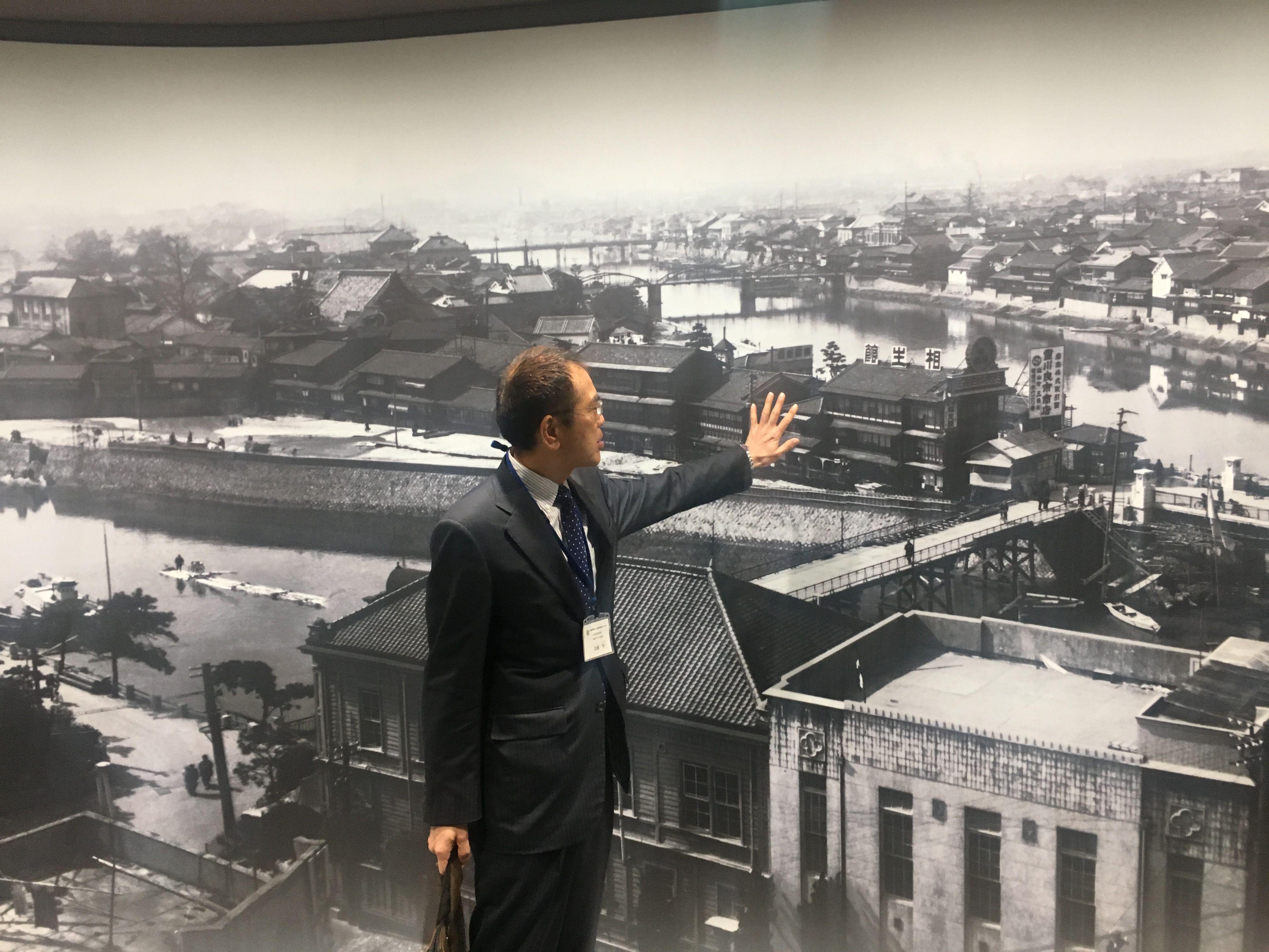 Muškarac rukom pokazuje na fotografiju Hirošime pre bombardovanja 