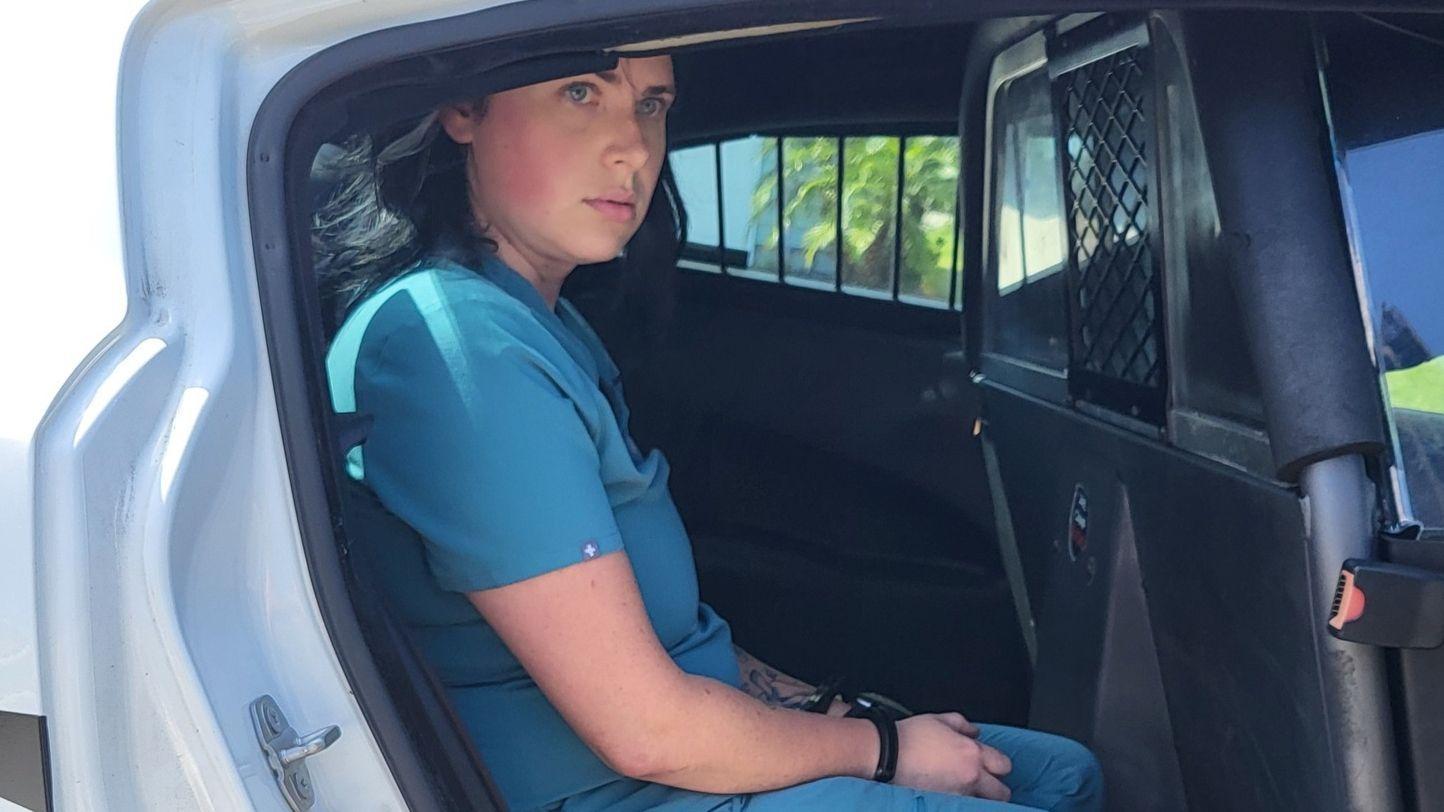 Žena u plavoj medicinskoj uniformi sa lisicama u policijskim kolima 