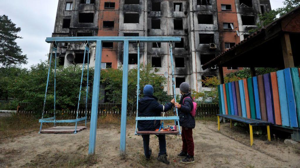 Kako se deca sa invaliditetom nose sa ratom u Ukrajini 8 Deca na igralištu gledaju u spaljenu zgradu od bombardovanja 2022. godine