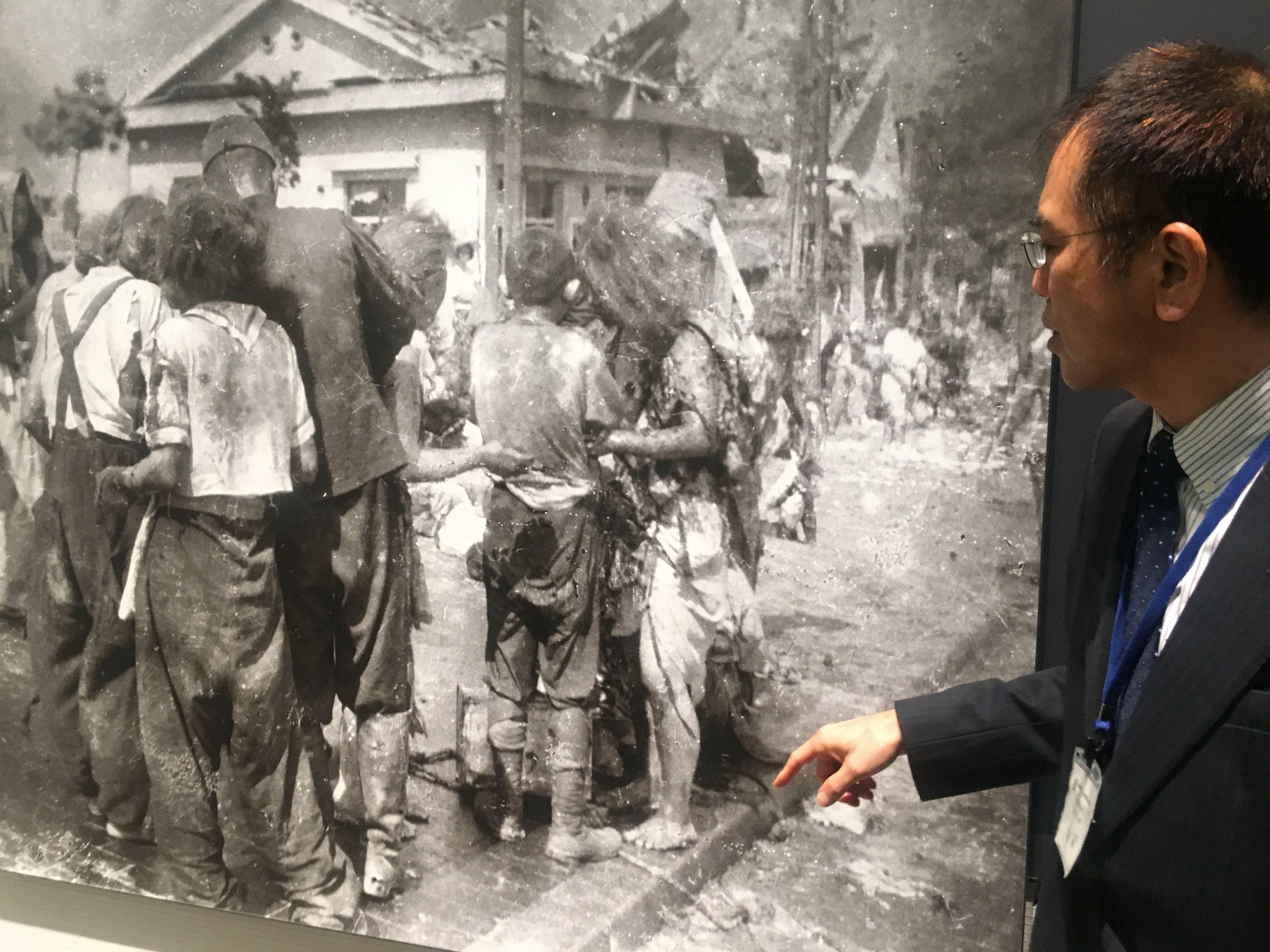 Muškarac stoji pored fotografije dece koja stoje u gomili posle atomske bombe u Hirošimi