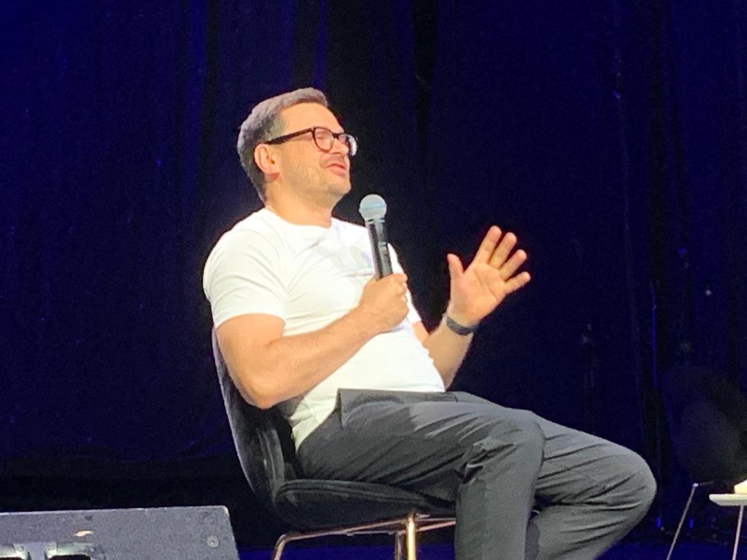 Ilja Jašin u Beogradu: Ne odustajemo od slobodne Rusije 1 Ilja Jašin sedi na stolici na bini u beloj majici i sivim pantalonama, i priča u mikrofon, nosi naočale i ima tamnu kosu