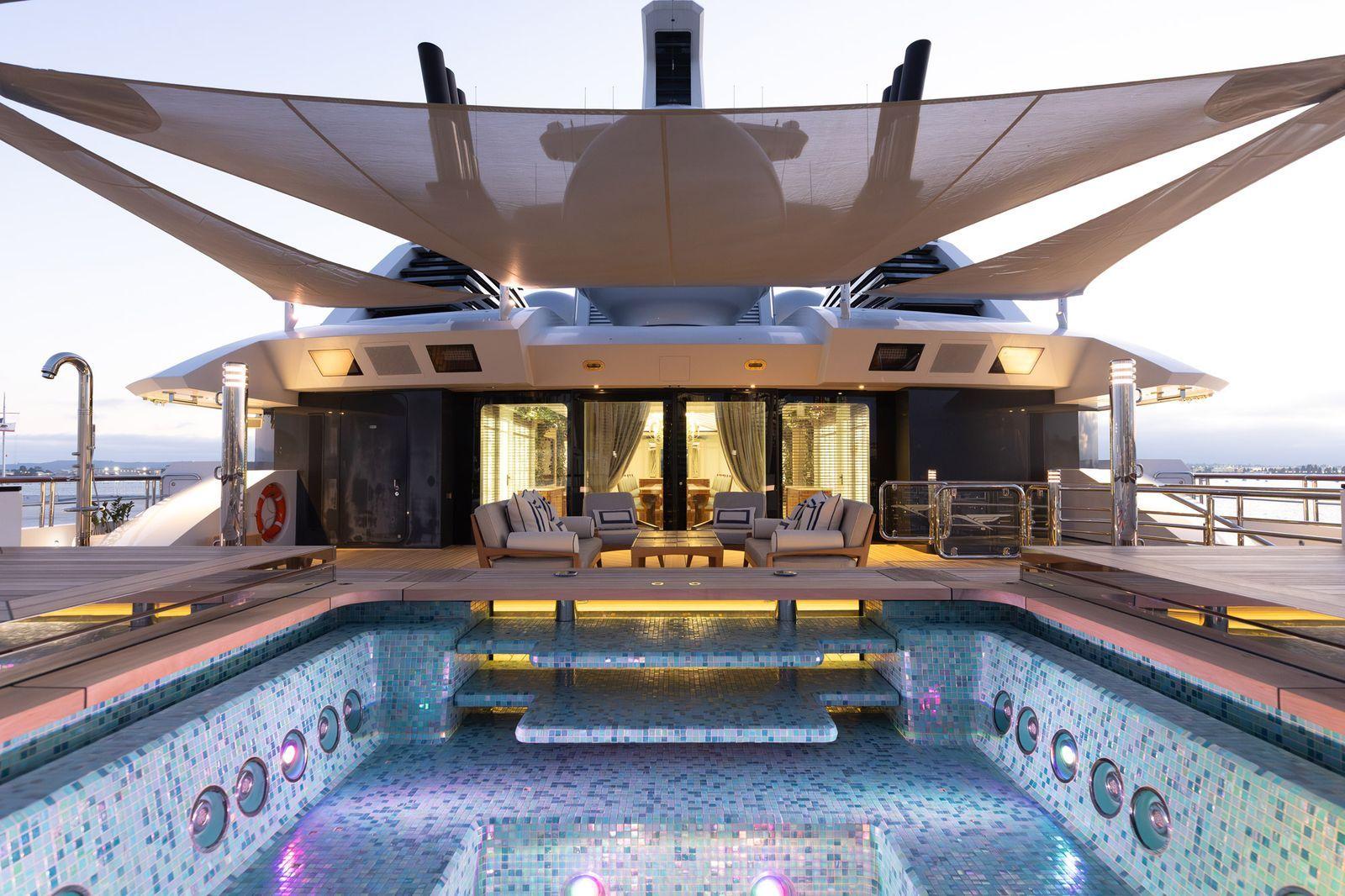 'Beskonačni' bazen, helidrom, osam soba: 'Superjahta ruskog milijardera' na aukciji 1 Bazen na jahti Amadea, sa malim tamnoplavim i svetloplavim pločicama. Bazen je prazan. Na vrhu fotografije je veliki suncobran iznad bazena, a u pozadini je osvetljena soba sa zavesama otvorenim preko prozora. Fotelje se nalaze na vrhu, proširenom delu pored bazena.