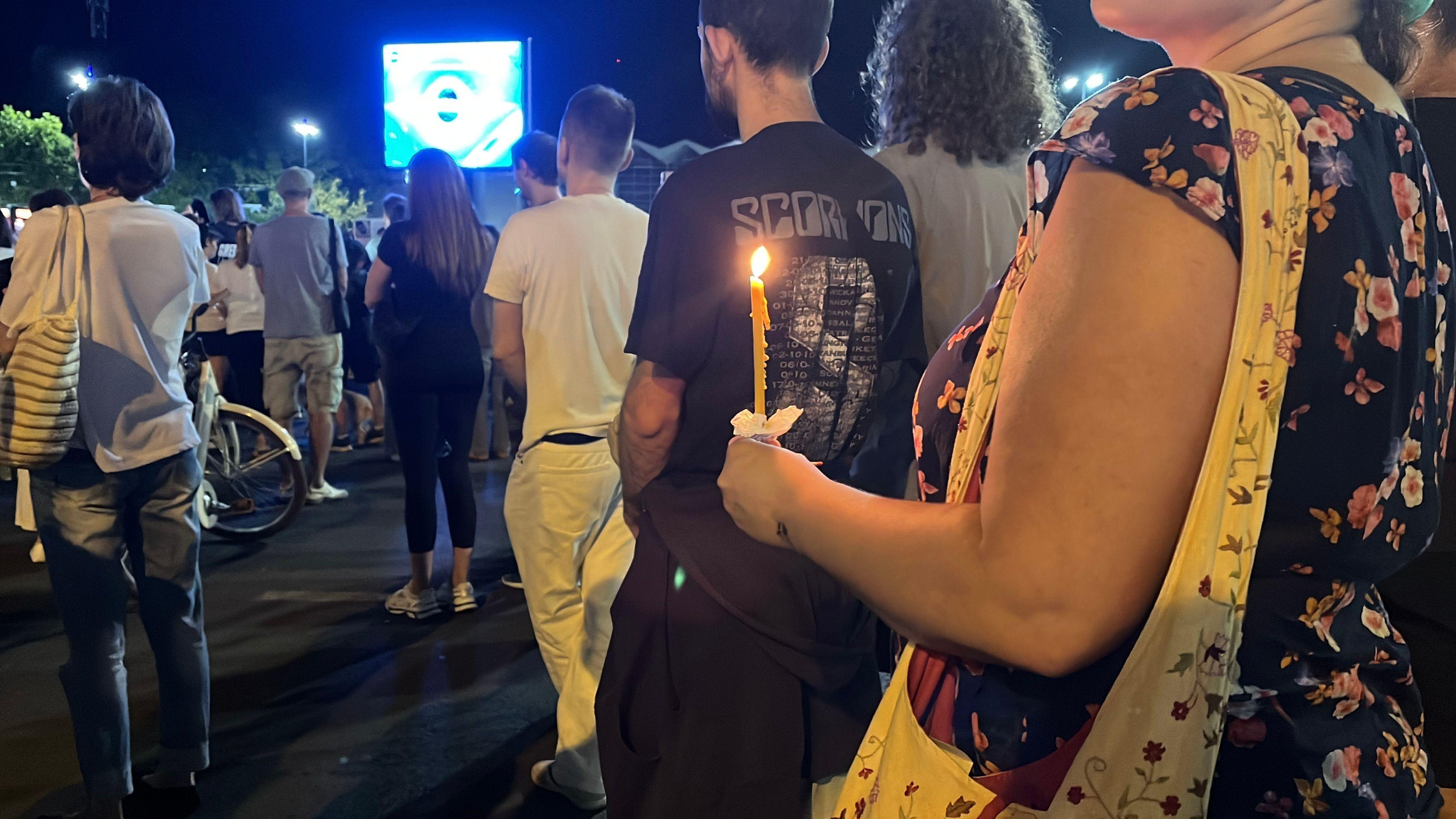 Žena koja drži sveću u ruci stoji zajedno sa drugim demonstrantima