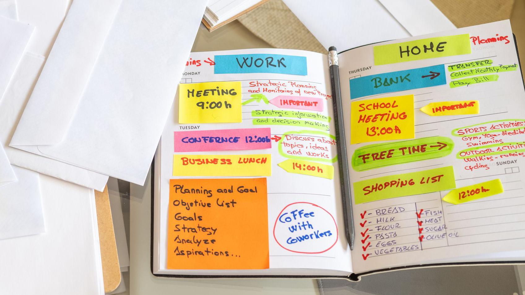Borite se sa moždanom maglom? Četiri saveta kako da je pobedite. 2 Person is organizing their work and personal agenda in a notebook at home, using sticky notes and colorful markers to plan their week, surrounded by envelopes, a smartphone, and a notepad