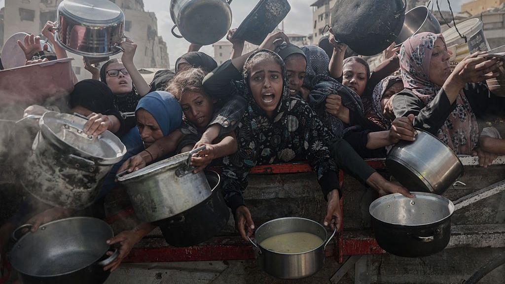 Šta je genocid 3 Žene u Gazi u rukama drže lonce sa hranom čekajući pomoć