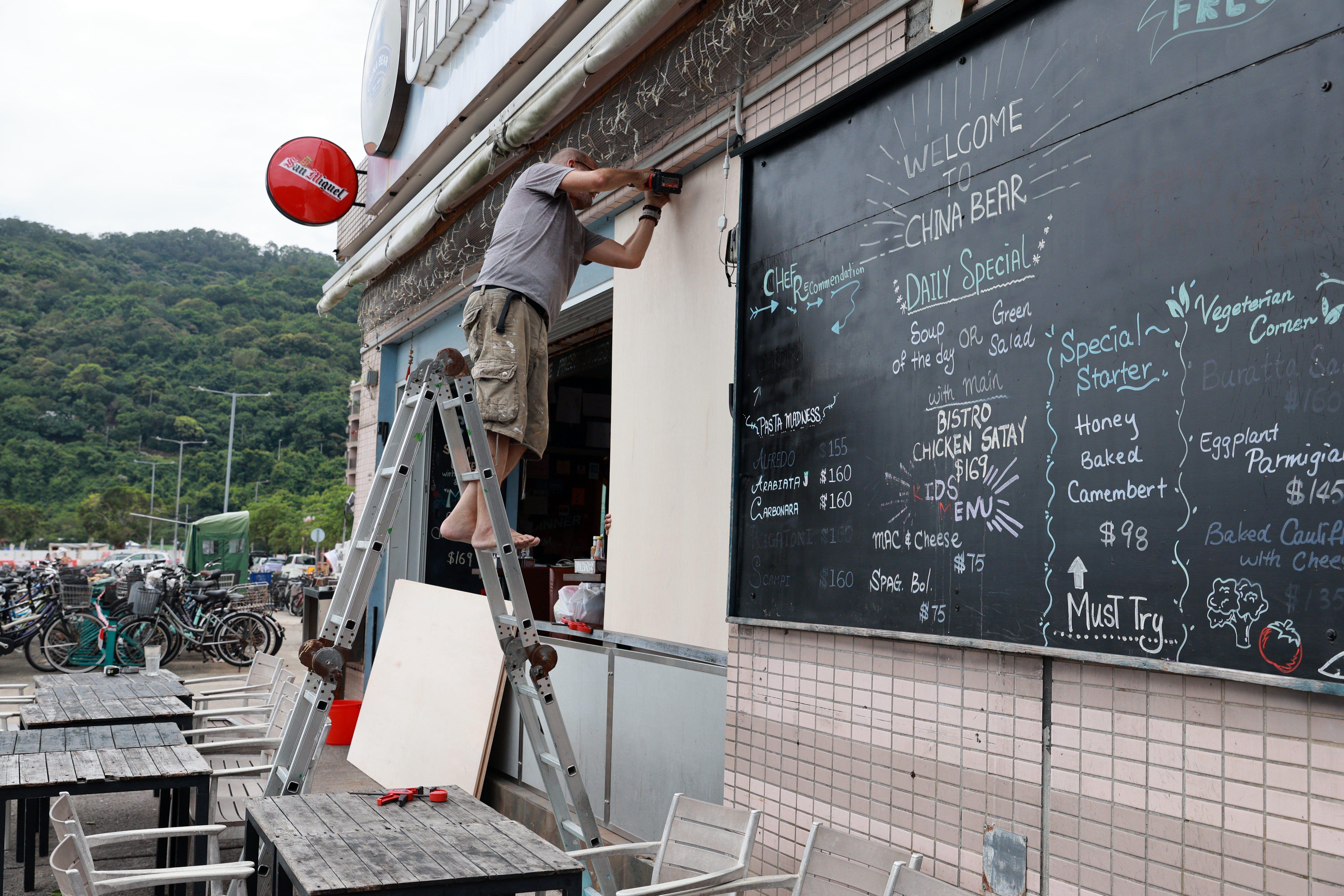 kina, tajfun ide ka kini, nevreme, muškarac zakucava drvene ploče kao zašzita od nevremena