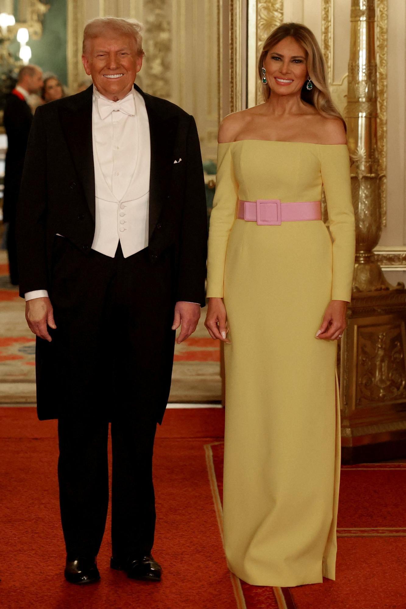 Melanijin šešir, žuta haljina i zlatna toaleta princeze Kejt - najzapaženiji modni trenuci Trampove posete 2 Donald Tramp nosio je frak, u skladu sa najvišim stepenom formalnog oblačenja - crni duži sako i pantalone, bela košulju sa kragnom u obliku krila, beli prsluk i bela leptir mašnu.
Melanija Tramp nosila je dugu, lepršavu žutu haljinu do poda, sa ravnim dekolteom koji otkriva ramena. Haljina je u struku bila stegnuta upadljivim, nežno roze kaišem.
