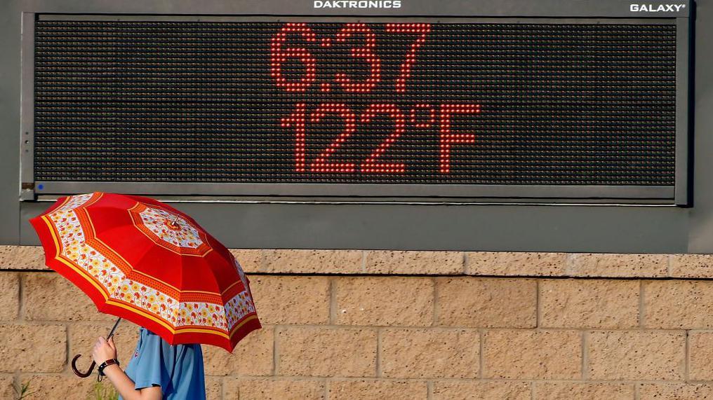 Kako ekstremne vrućine 'tope' naš DNK i ubrzavaju starenje 2 Osoba nosi kišobran umesto suncobrana prolazi pored oglasne table na kojoj je prikazana temperatura od 122 stepena Farenhajta