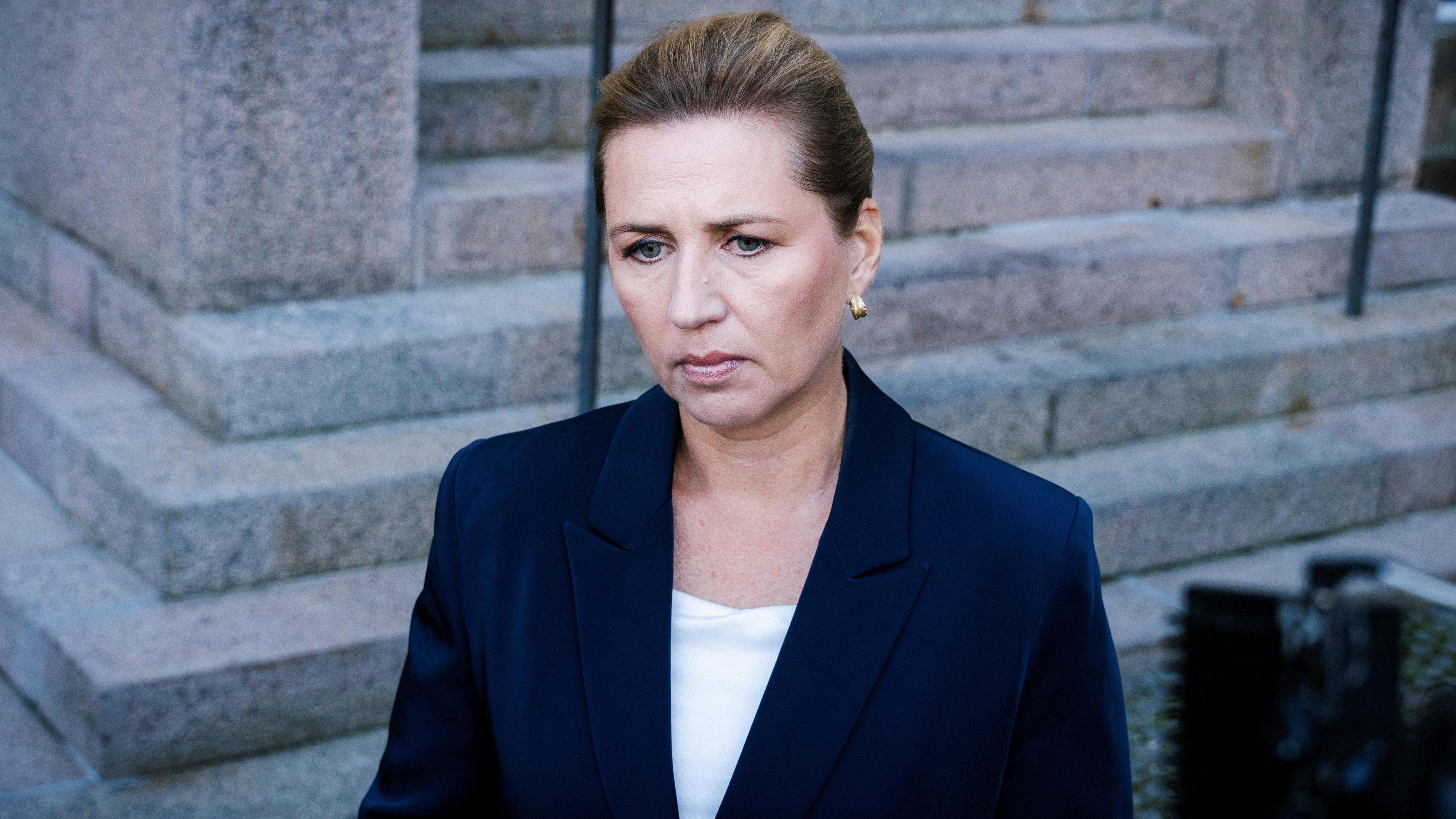 Dronovi zaustavili aerodrom u Kopenhagenu, premijerka ne odbacuje umešanost Rusije 1 Danska premijerka Mete Frederiksen stoji ispred kamenih stepenica obučena u tamnoplavi sako. Kosa joj je začešljana unazad, a izraz lica je ozbiljan.