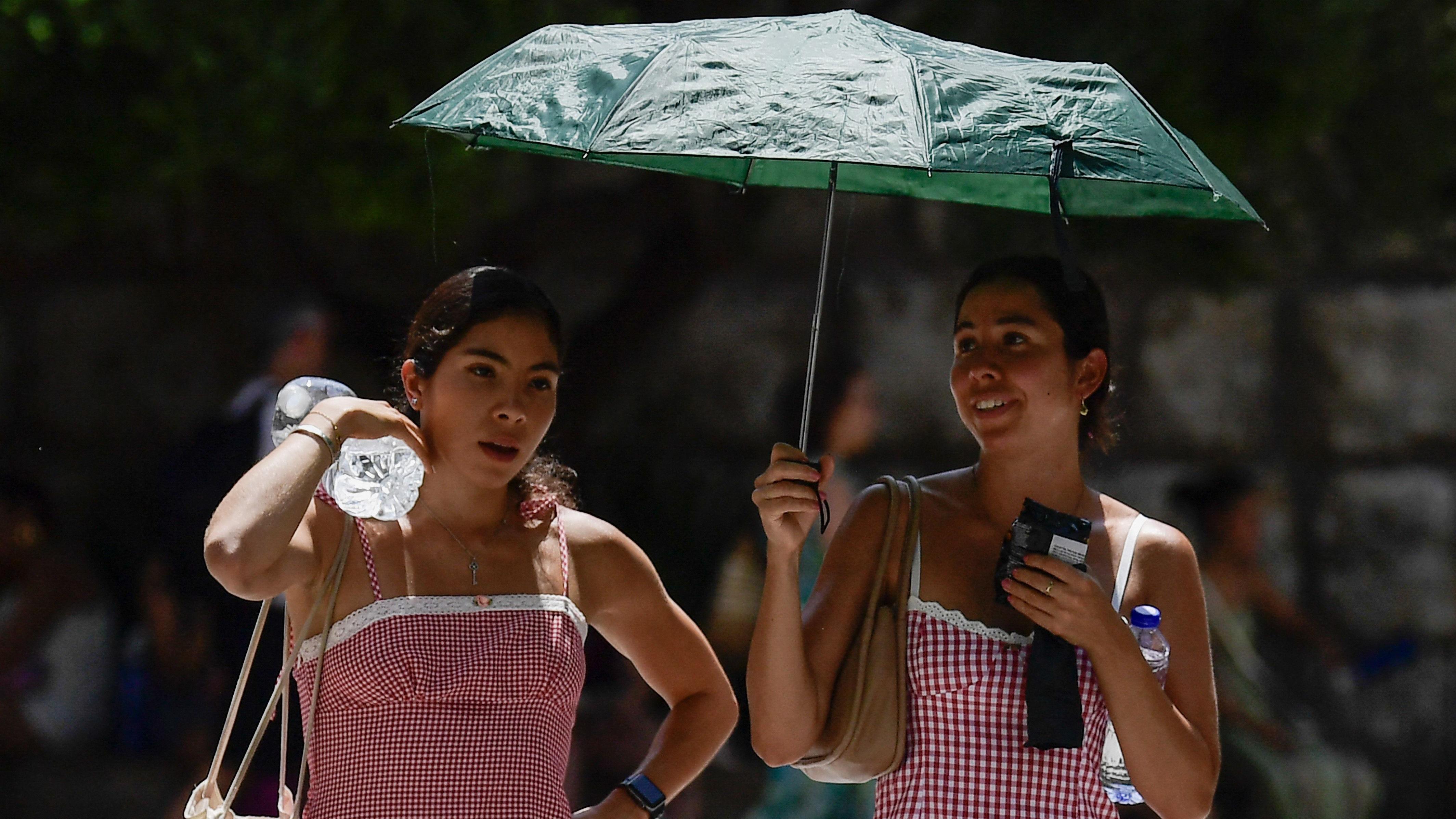 Kako ekstremne vrućine 'tope' naš DNK i ubrzavaju starenje 1 Dve mlade žene nose flaše vode i telefone sklonile su se od vrućine pod kišobranom