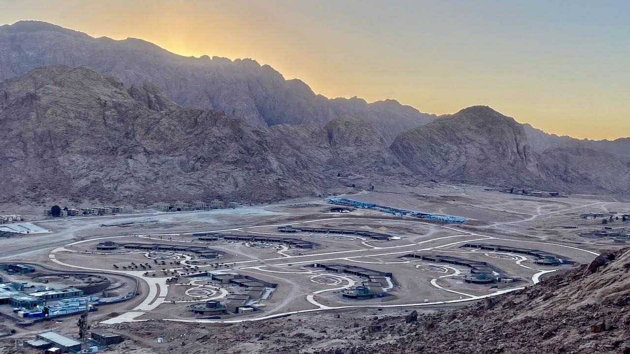 Pogled na jedan od objekata, koji je još u izgradnji, ravnica el-Raha. Sunce je iza okolnih planina, dok je gradilište u prvom planu, sa putevima koji povezuju različite zgrade.