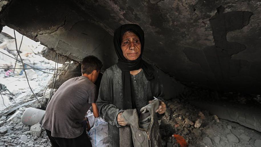 BBC i drugi mediji traže od Izraela da pusti strane novinare u Gazu 1 Žena u sivoj odeći sa crnom maramom na glavi stoji ispod ruševine. Iza nje dečak