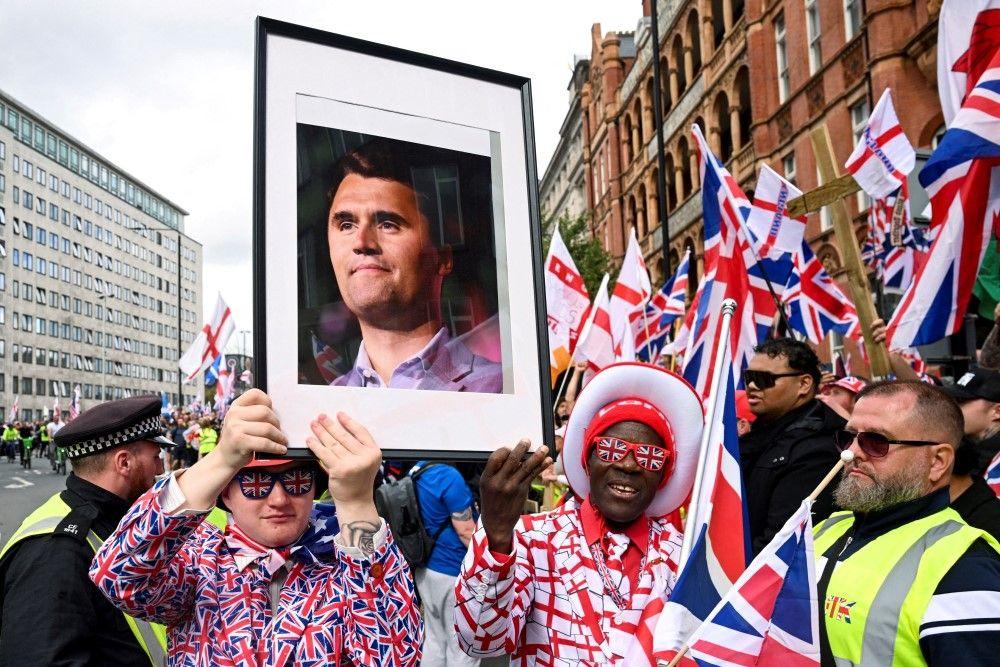 protest u londonu, čarli kirk, charlie kirk, muškarac u odelu u bojama zastava velike britanije nosi sliku sa likom Čarlija Kirka ubijenog konzervativnog aktiviste iz Amerike