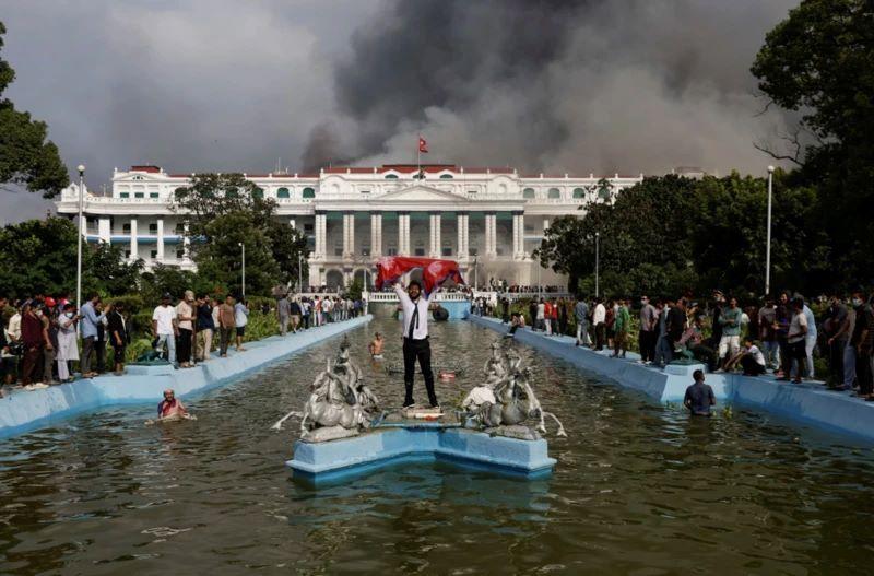 Nepal: Vojska uspostavila mir, prva žena premijer u istoriji zemlje 7 Muškarac slavi držeći zastavu Nepala ispred zgrade parlamenta iz koje izbija dim