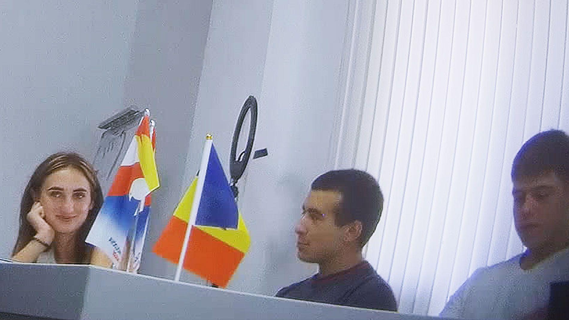 Žena sa dugom braon kosom (Alina Juk) smeši se grupi muškaraca koja je okružuje. Svi sede za dugačkim stolom na kome su dve zastava, od kojih je jedna moldavska sa crvenom, žutom i plavom bojom 