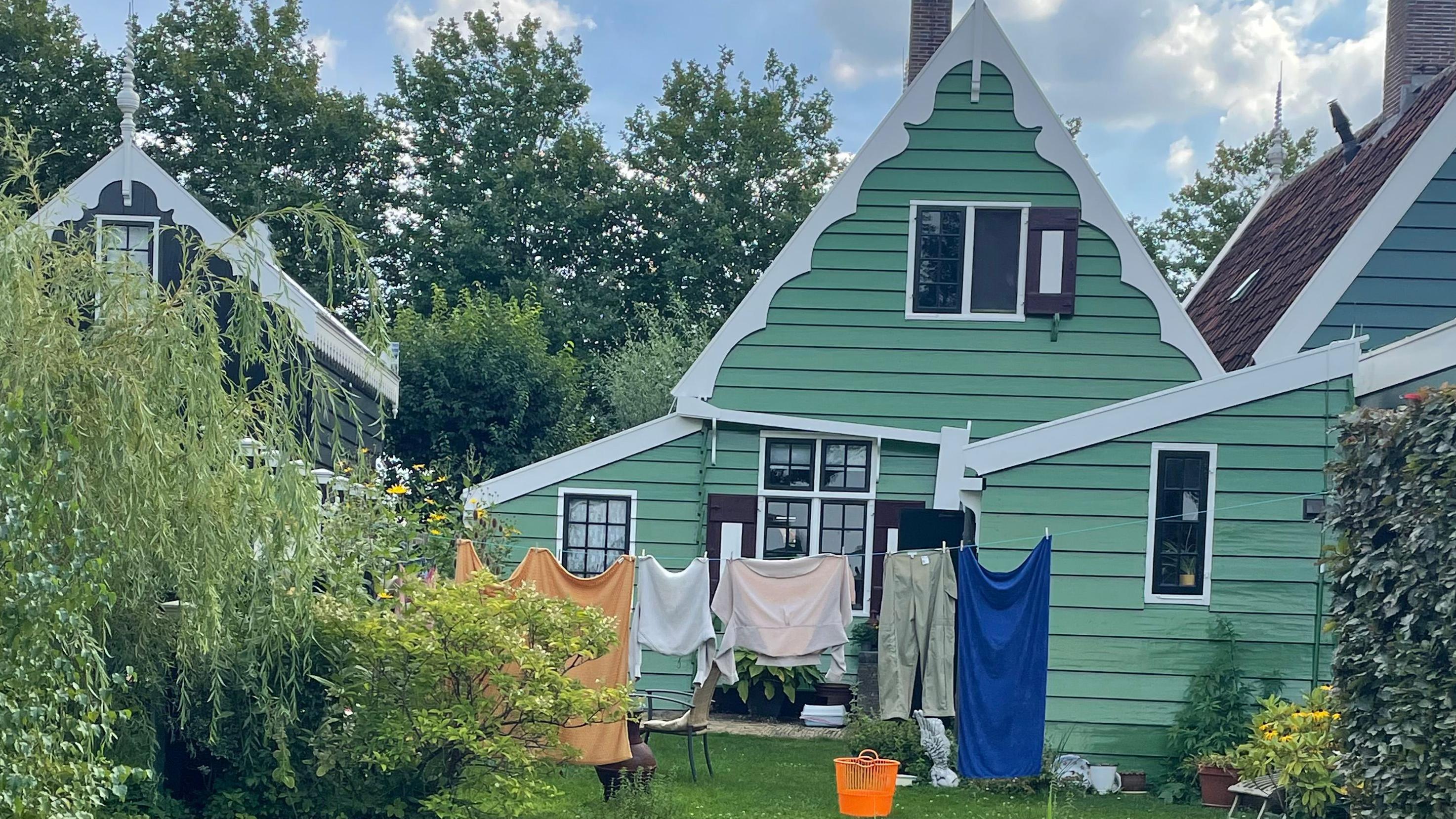 Da li biste platili 17,5 evra da gledate vetrenjače 2 kuće ofarbane u zeleno. Ispred je žica za veš na kojoj je zakačena odeća