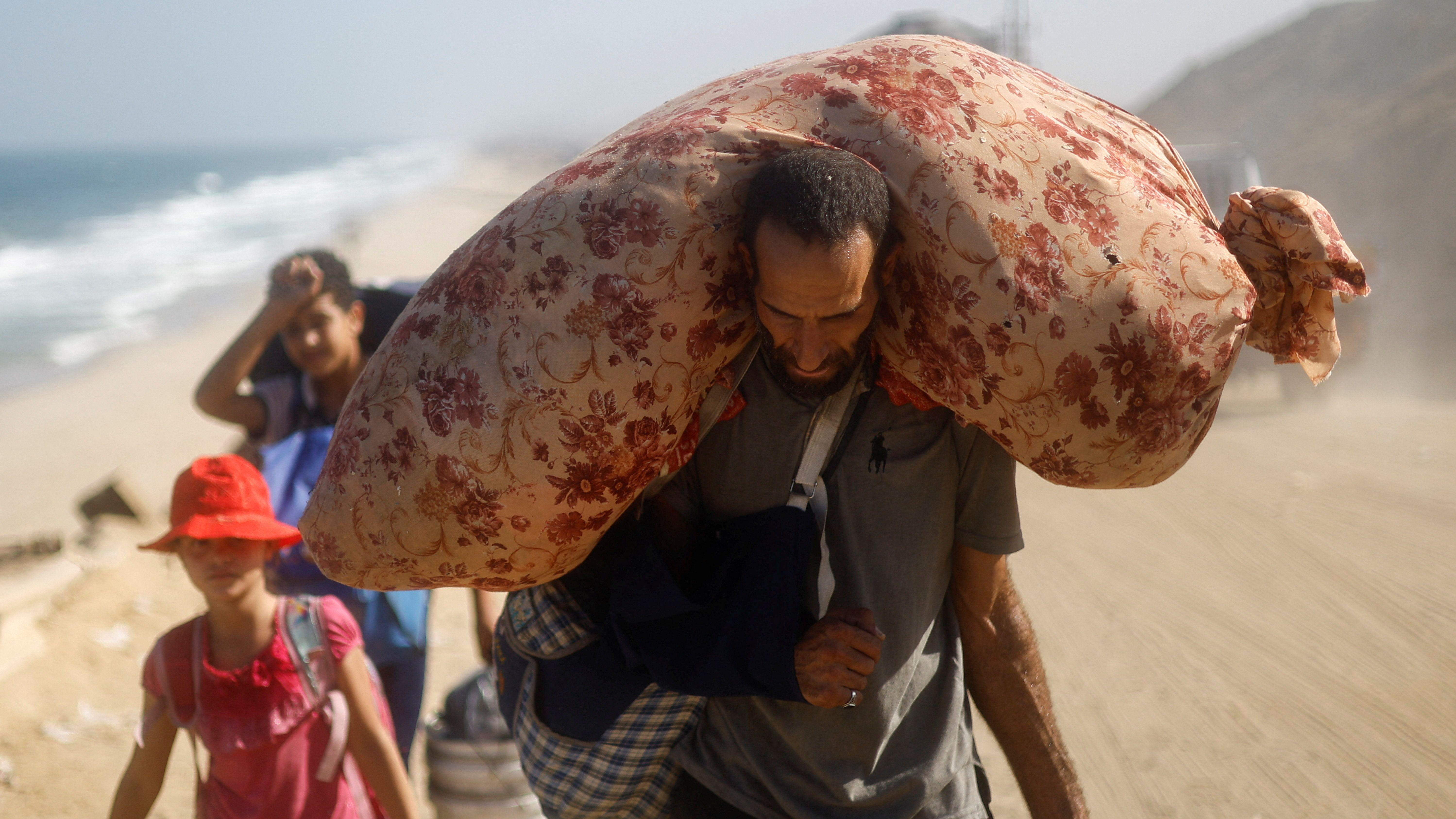 Muškarac sa povređenom rukom nosi ogroman džak na leđima, iza njega dečak i devojčica nose stvari